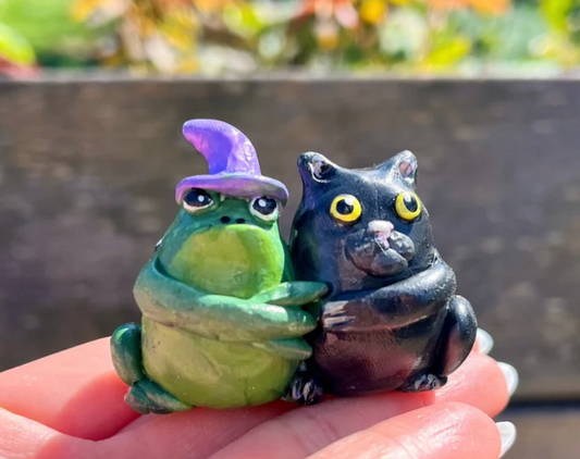 Black halloween cat hugging green toad with a purple witch hat